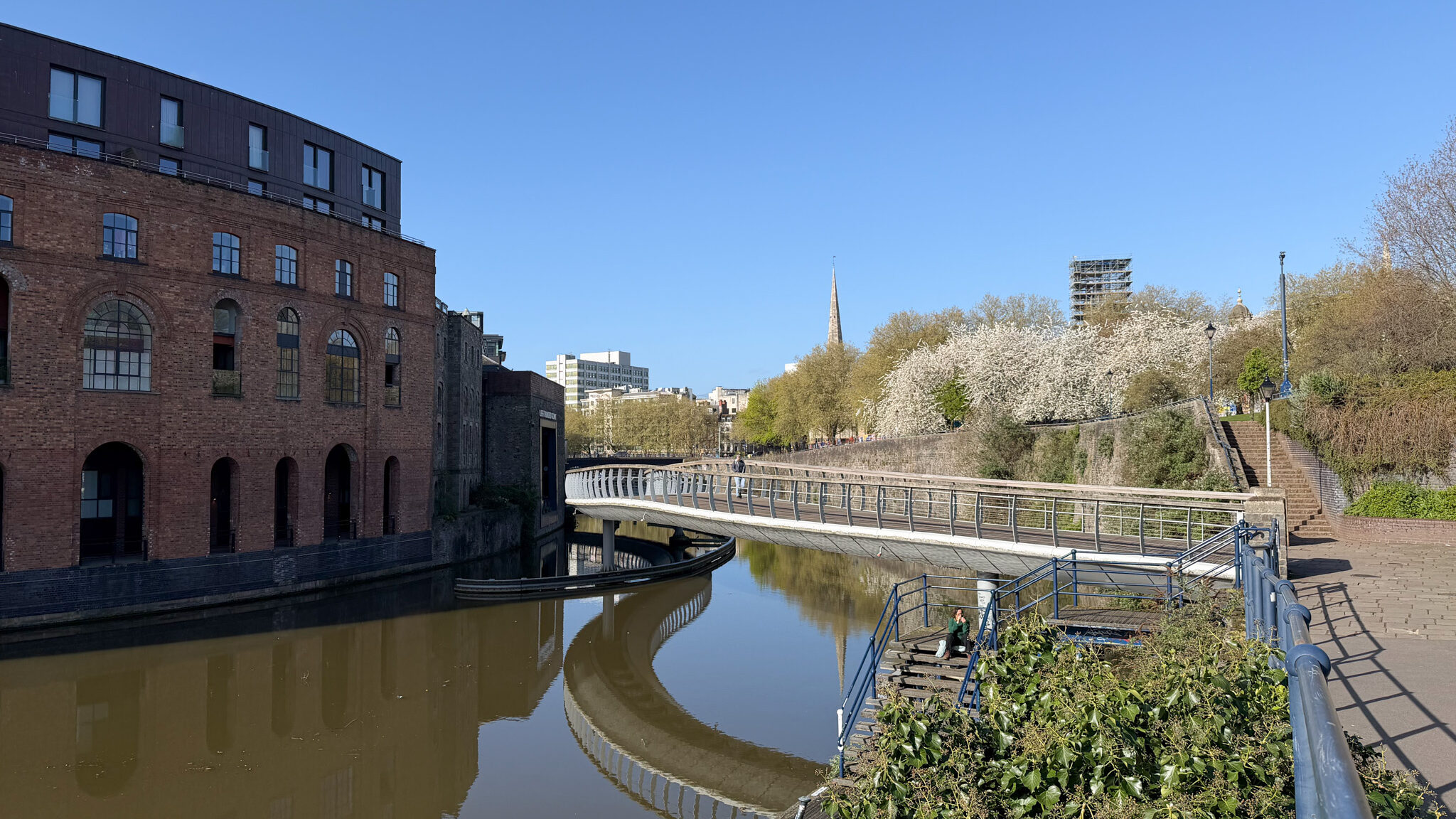 Brick industrial building along a canal with a curved railing and blue sky above.