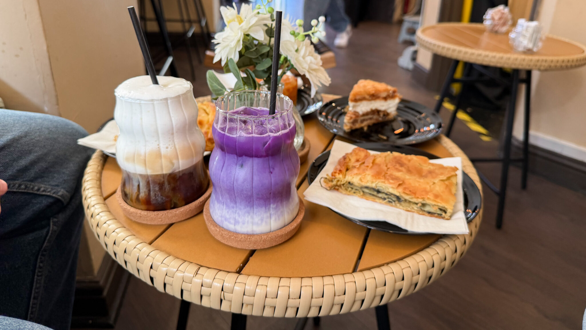 Two layered drinks in ceramic mugs with black straws sit on a round wicker table.