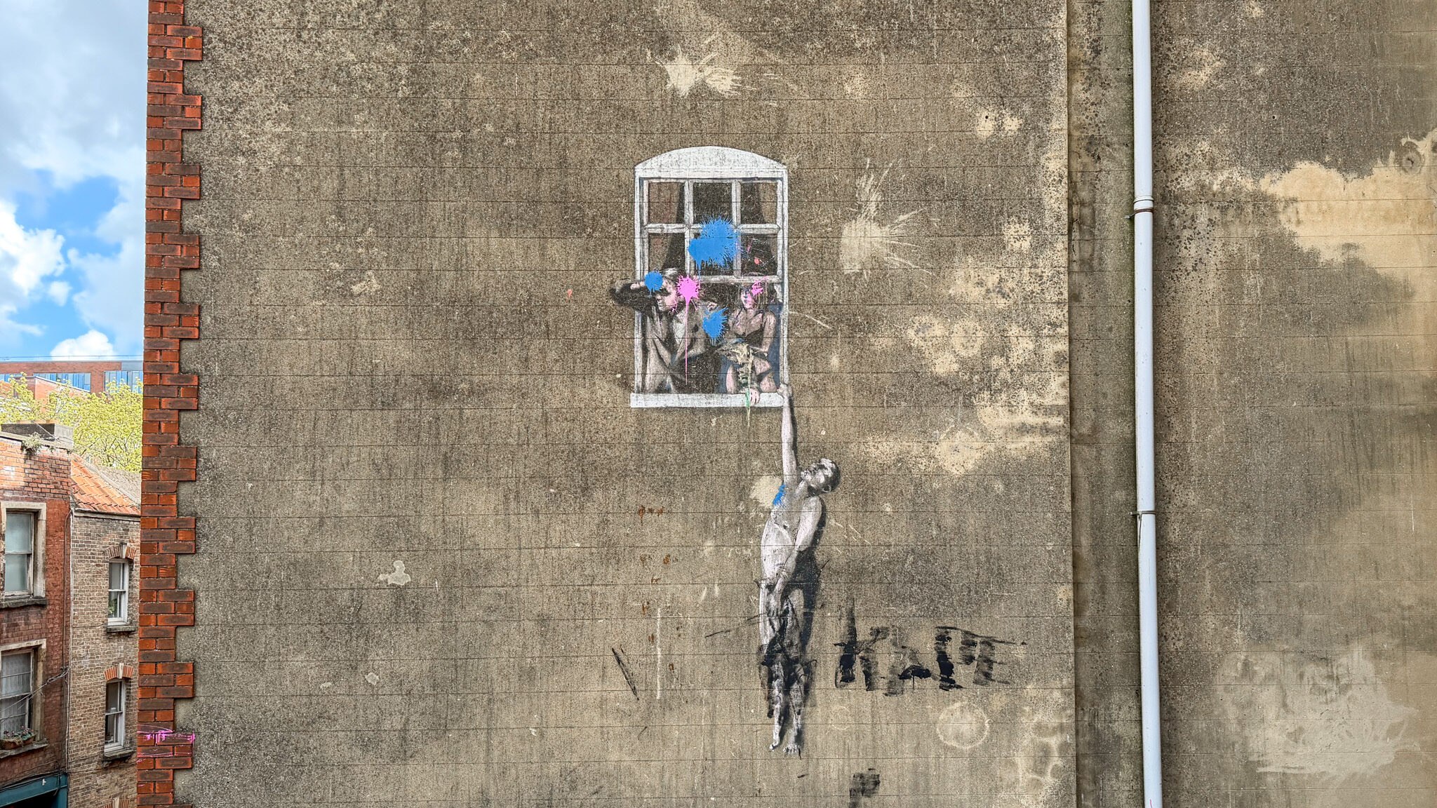 Graffiti of a man holding a window with blue and pink paint splatters on a worn concrete wall.