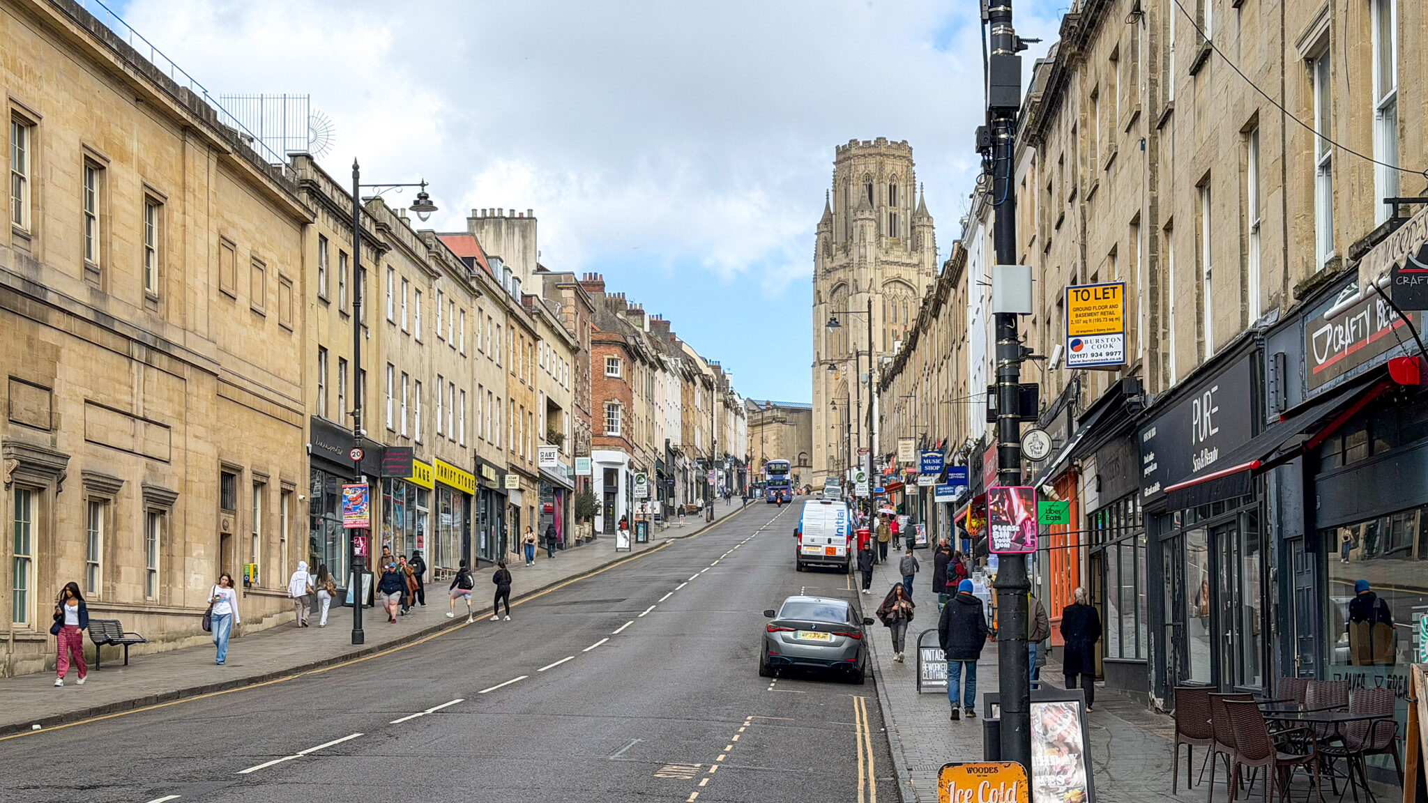 Downhill city street with sandstone buildings on cloudy day.