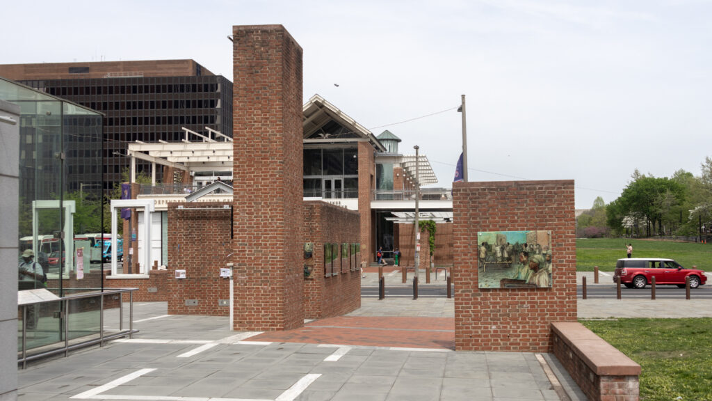 Brick-paved plaza flanked by brick walls and modern glass building on the left.