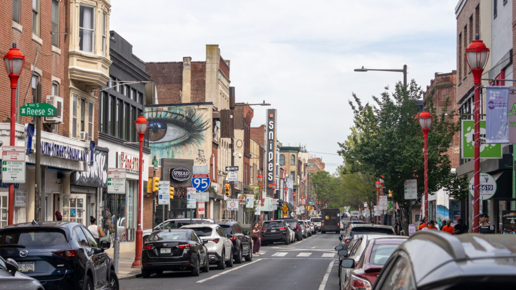 Busy urban street lined with storefronts, parked cars, and red lampposts.