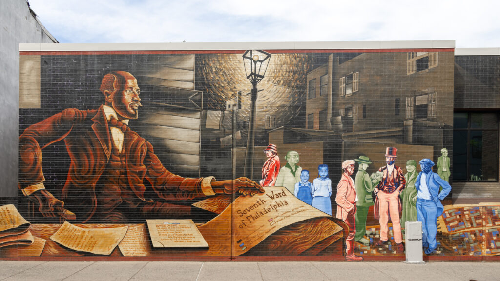 Mural depicting a large man in a red suit signing papers on the left, with a crowd of colorful people and cityscape on the right.