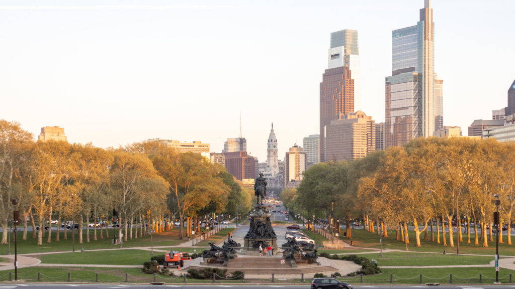 City park with a statue fountain in foreground and a modern skyscraper skyline in the distance.