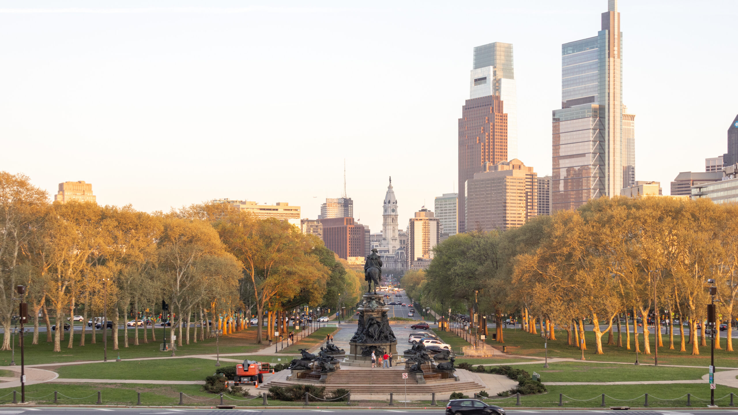 City park with a statue fountain in foreground and a modern skyscraper skyline in the distance.