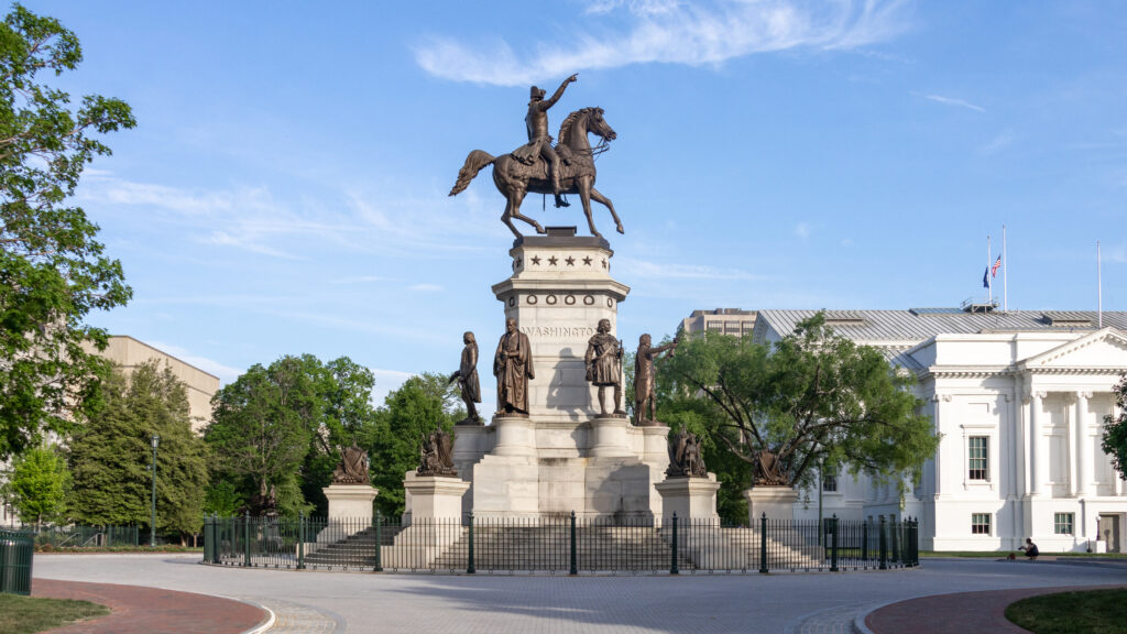 Statue of George Washington on a horse next to government building.