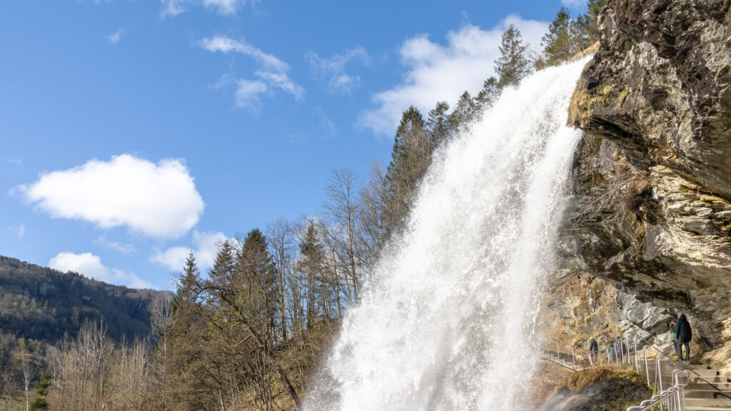 Large waterfall falling over rocks with walkway under it.