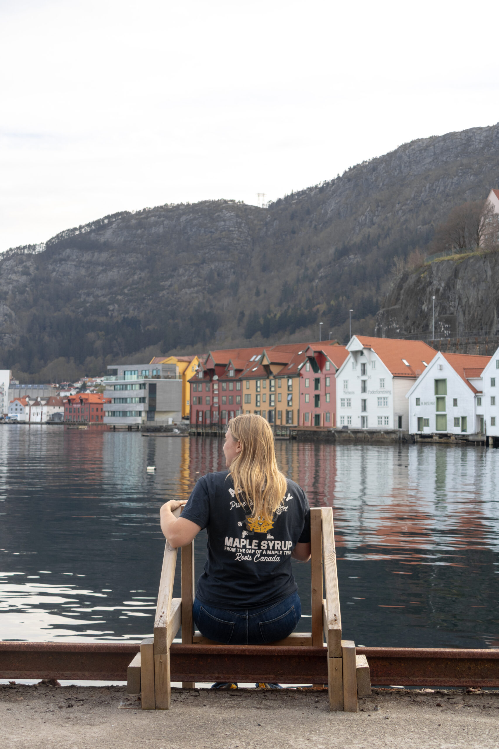 Woman sitting on wooden ladder next to water in Bergen.