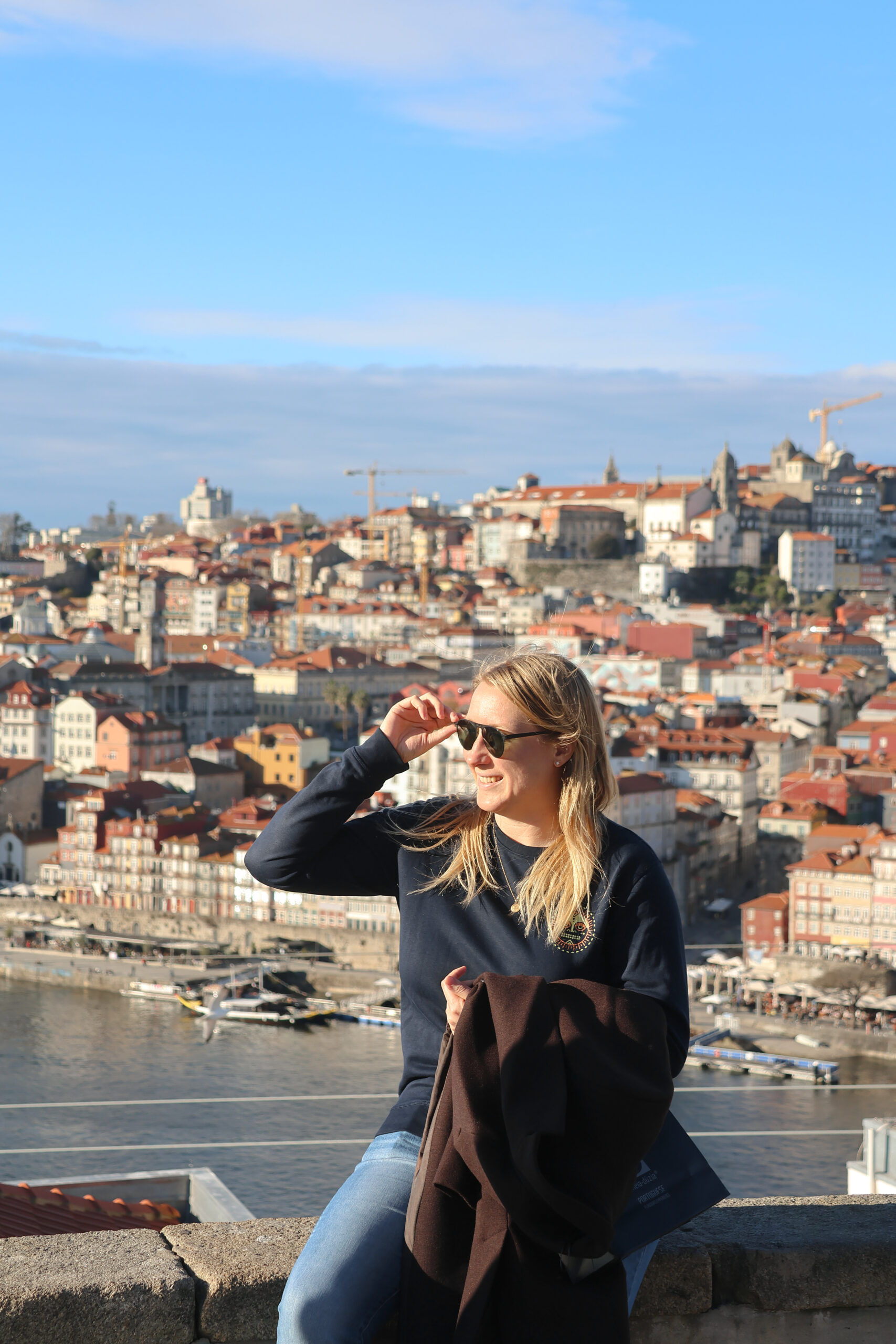 Girl with blonde hair sitting on wall above Porto.