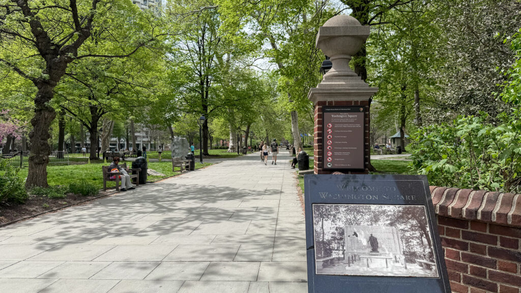 Washington Square Park: tree-lined walkway with benches and pedestrians.