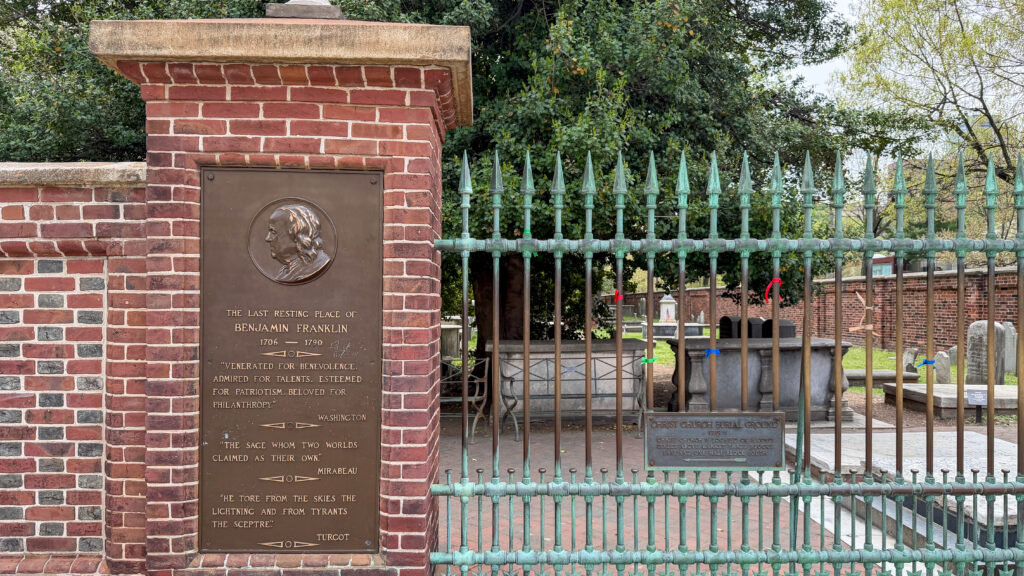 Bronze memorial plaque set in a red brick pillar at a cemetery entrance.