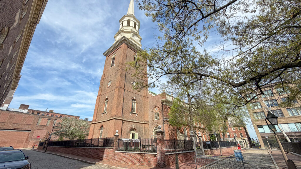 Brick church with a tall white steeple reaching into a blue sky.