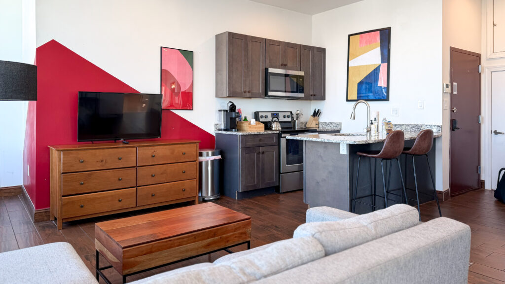 Open-plan living area with a kitchen island, dark wood cabinets, appliances, and two brown bar stools.