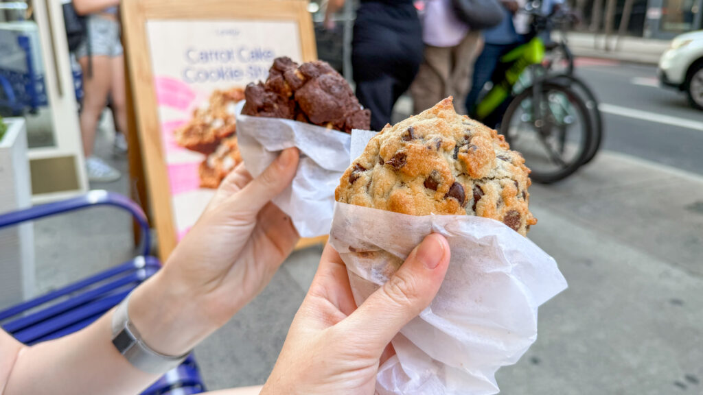 Two people hold parchment-wrapped cookies on street.