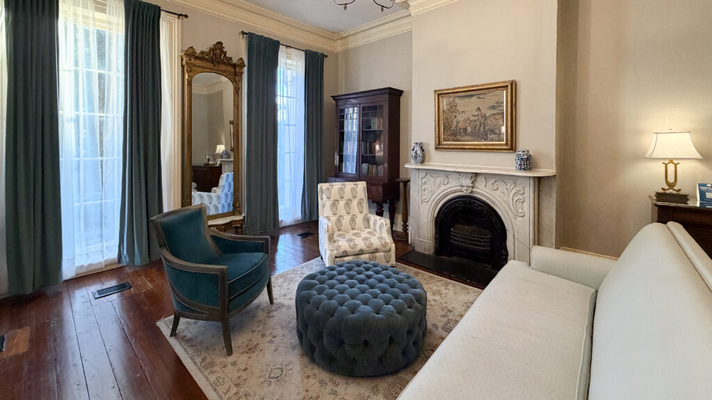 Elegant living room with dark green curtains, tall windows, and a carved mirror.