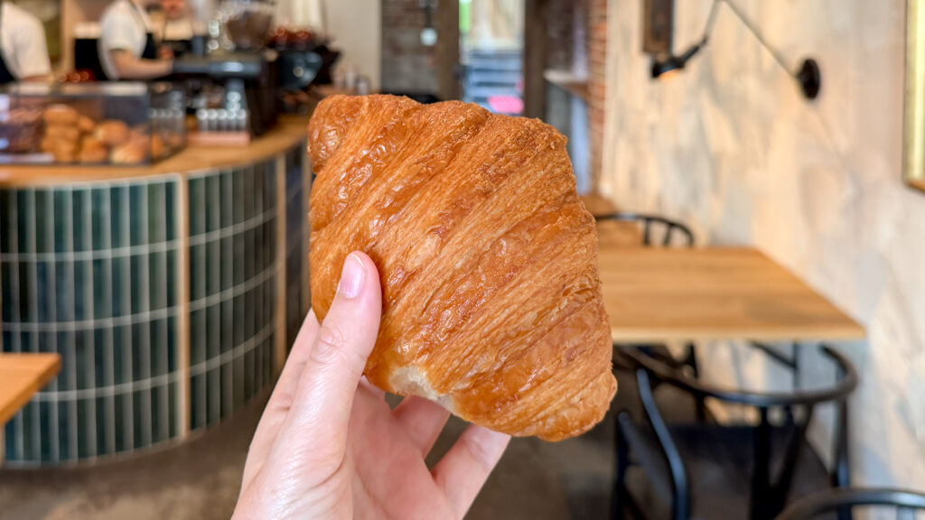 Close-up of a hand holding a flaky, golden croissant inside a cafe.