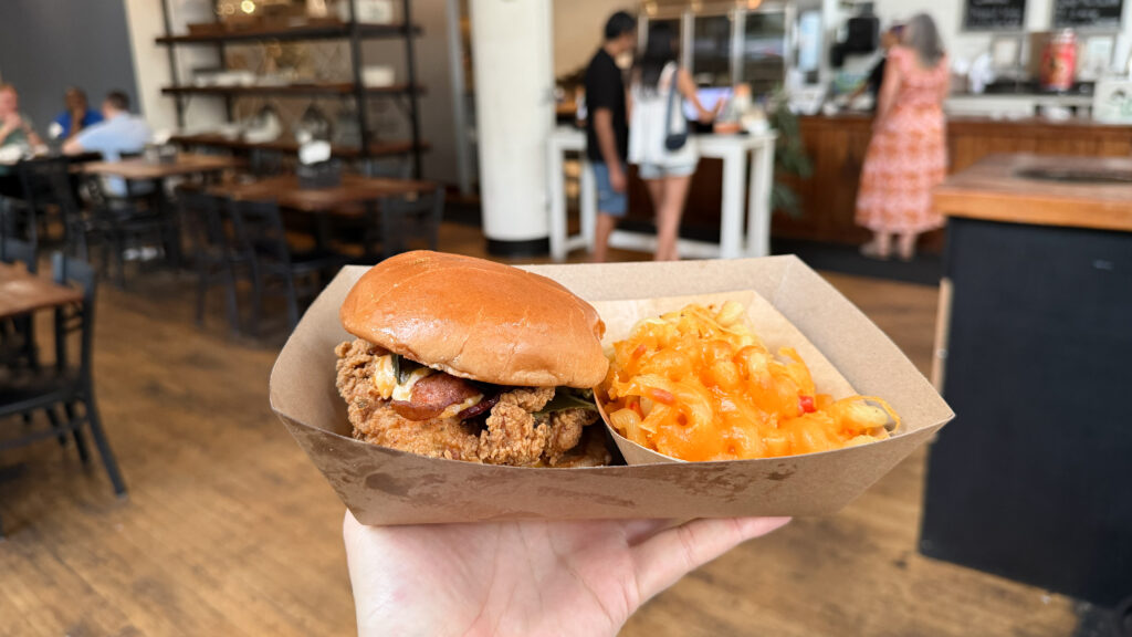Takeout box with a crispy fried chicken sandwich and macaroni and cheese.