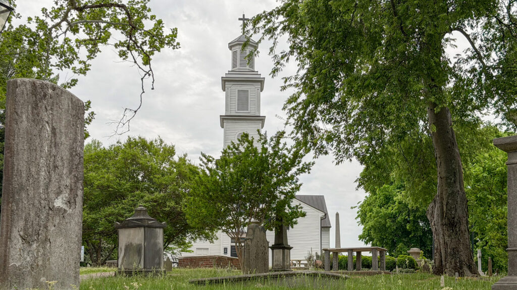 White church steeple visible beyond a graveyard with weathered headstones.