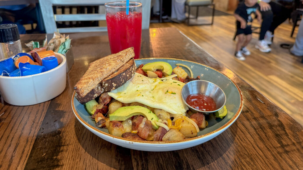 Big breakfast bowl with potatoes, eggs, toast, and vegetables.