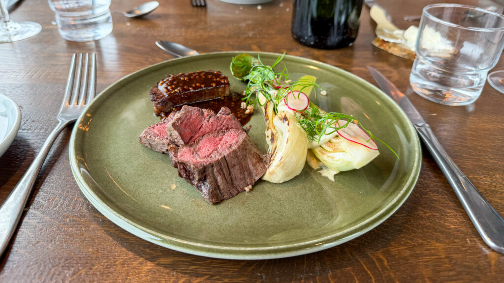 Sliced medium-rare beef with a glossy sauce, paired with grilled fennel and fresh greens.
