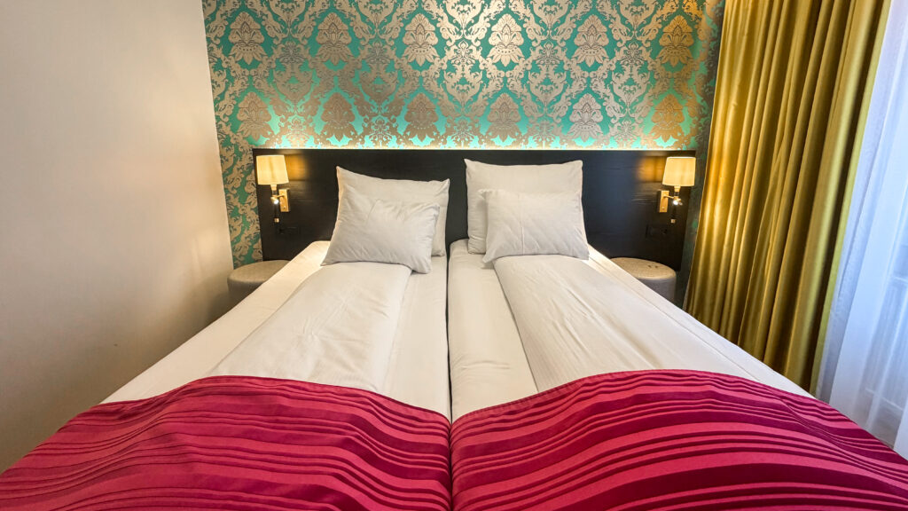 Double bed in a hotel room with white pillows and a red striped blanket.