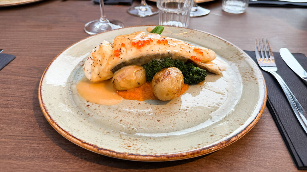 Salmon fillet with orange roe atop a bed of greens and potatoes.