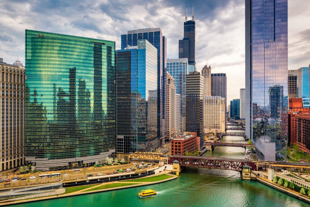 Downtown Chicago skyline along the river with glass skyscrapers and a small yellow boat on the water.