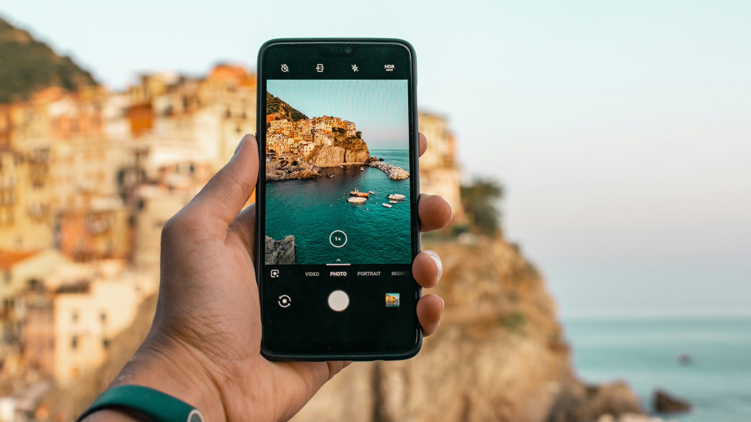 Persona holding smartphone to take photo of cliffside town.