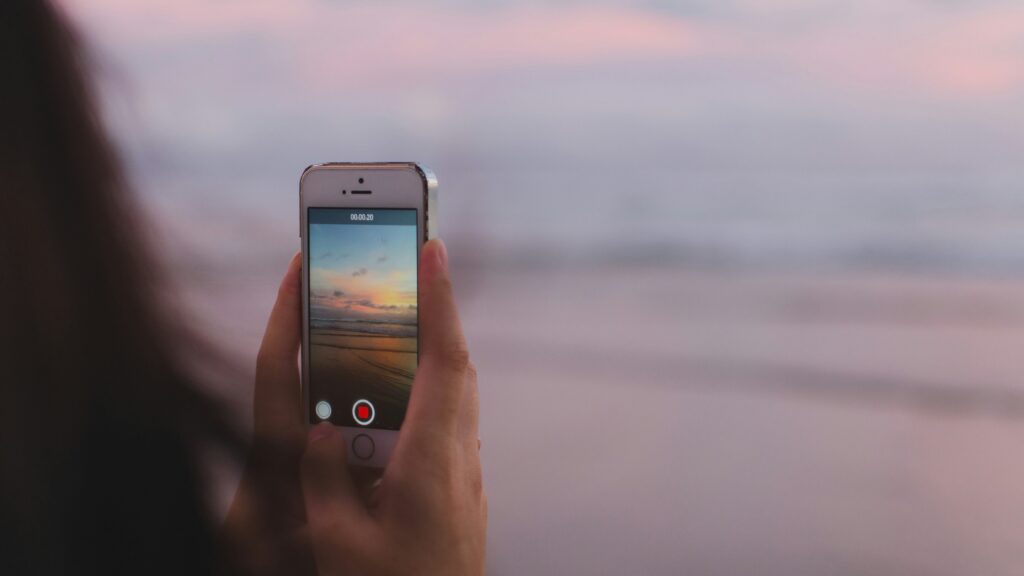 Phone Security | Krista the Explorer Person holding a smartphone to record a sunset on the beach.
