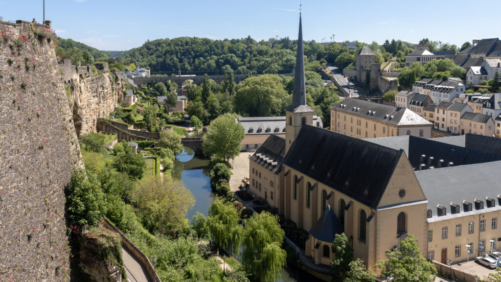 Grund Luxembourg | Krista the Explorer Panoramic view of a historic town with castle walls, a river, and a tall church.
