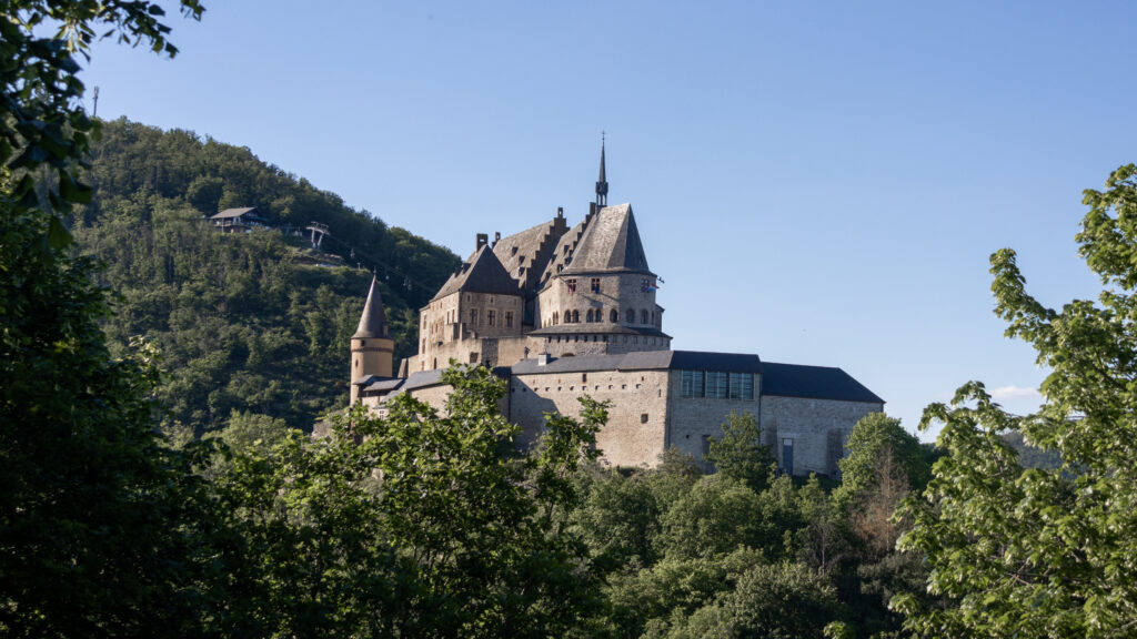 Stone castle with spire and crenellated roofs perched on a green hillside.