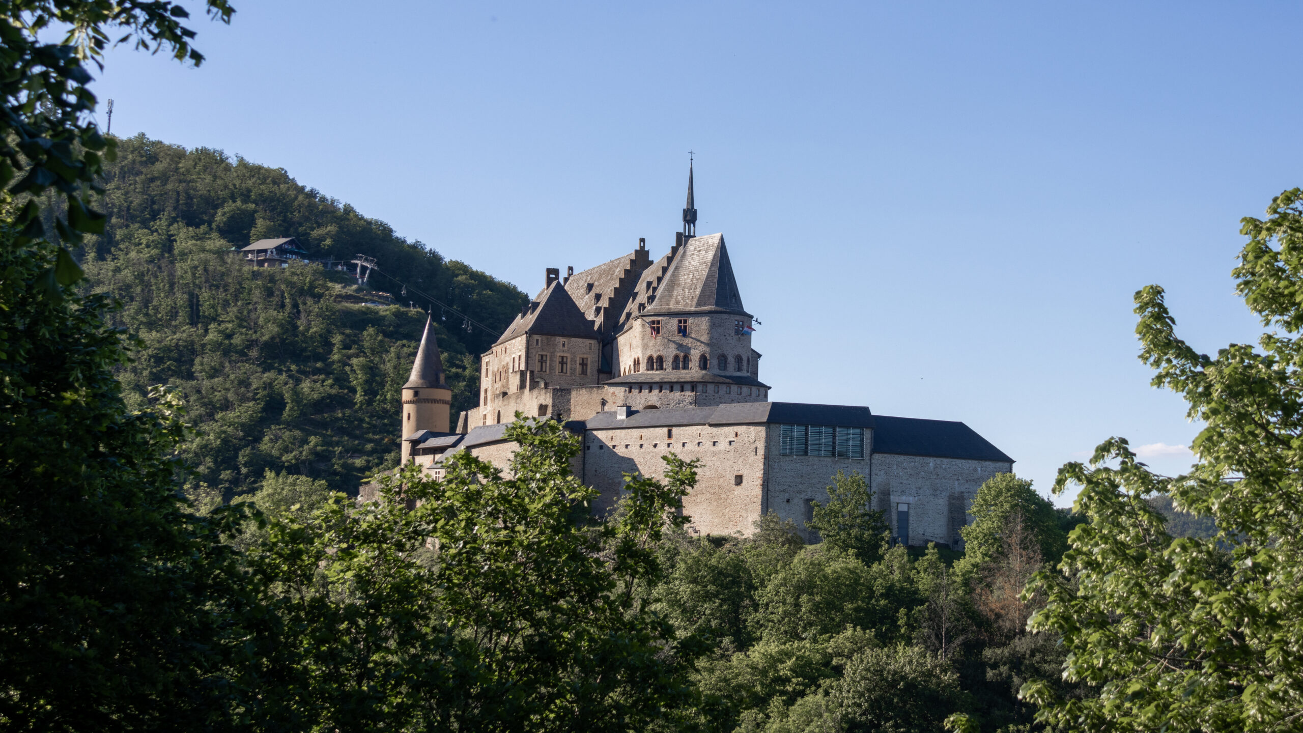 Stone castle with spire and crenellated roofs perched on a green hillside.