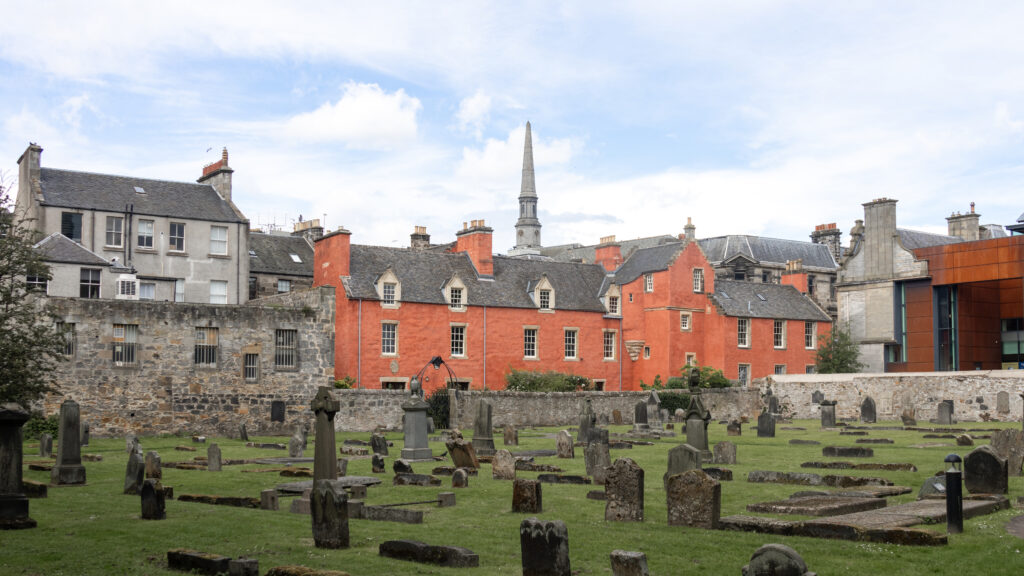 Abbot House Dunfermline | Krista the Explorer Gravestones in a cemetery with a stone wall and red-brick building.