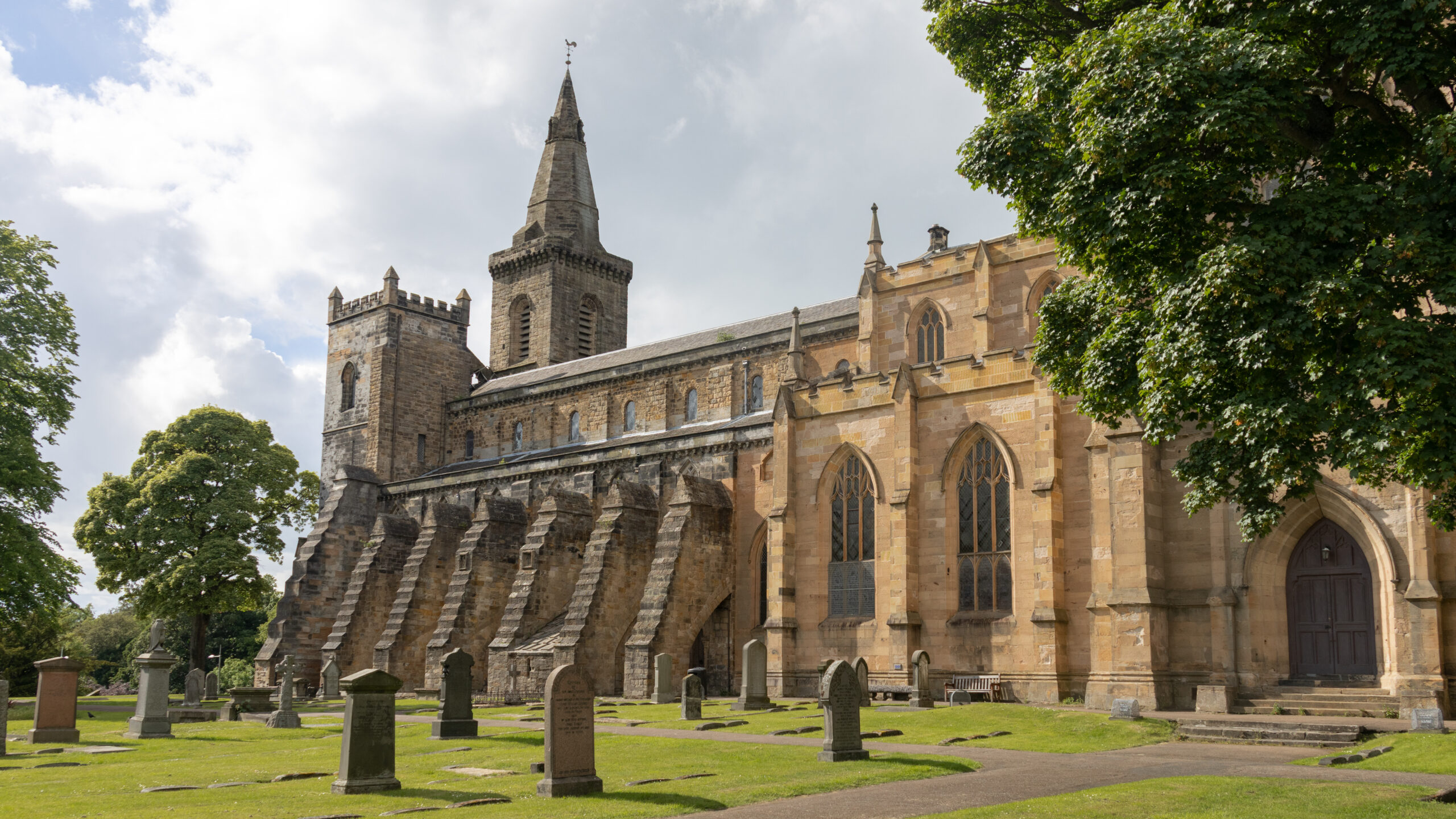 Stone church with a tall spire and surrounding graveyard.