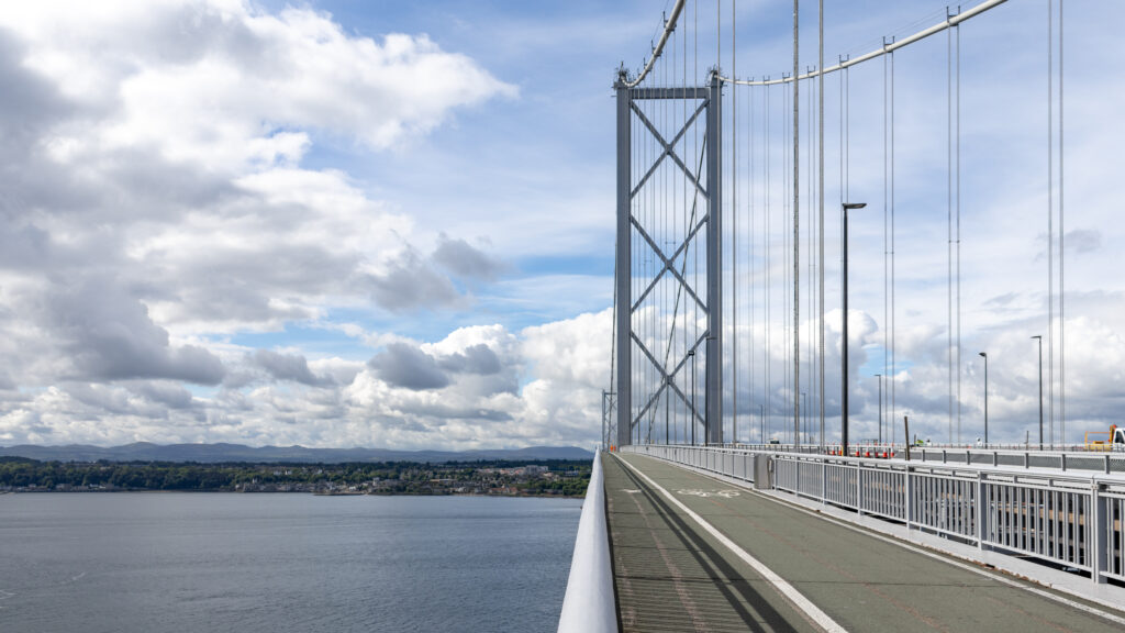 Suspension bridge over a wide river with a pedestrian walkway.