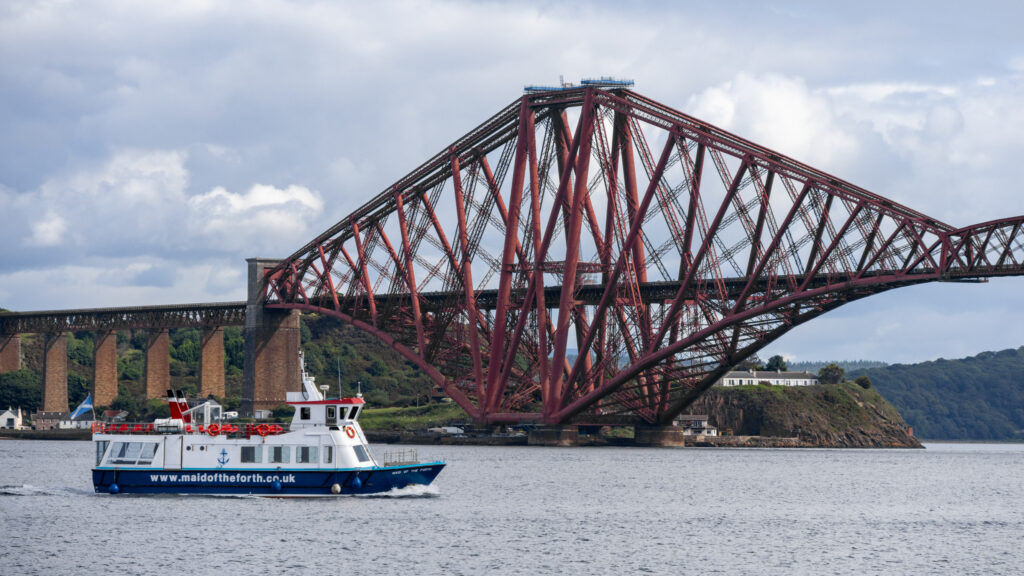 Tour boat passing in front of steel rail bridge.