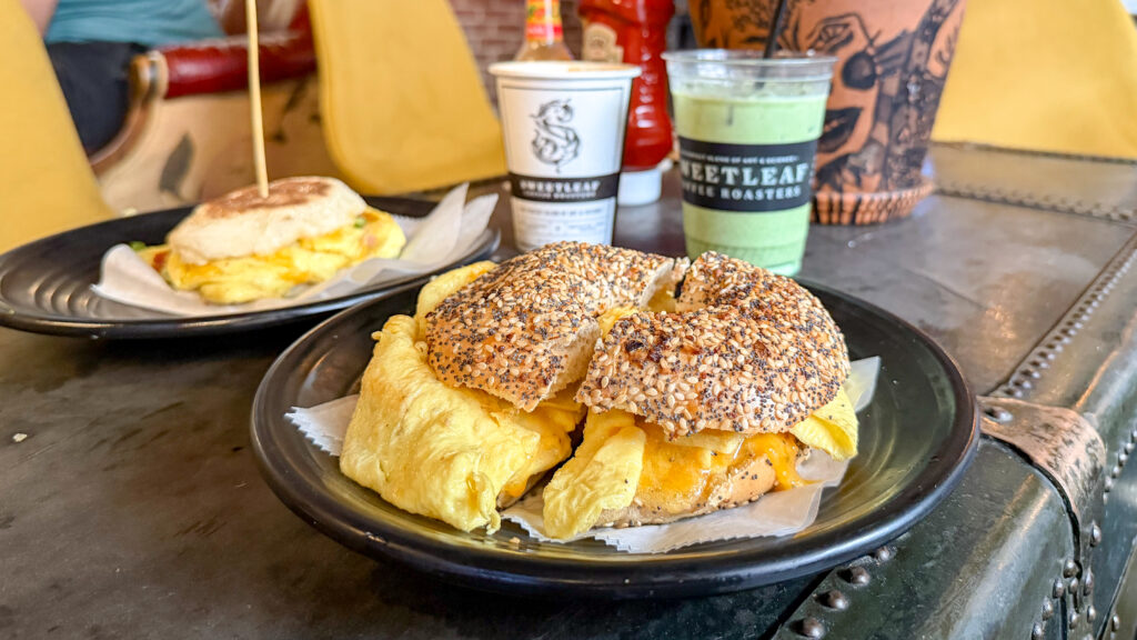 Sweetleaf Coffee Roasters Brooklyn | Krista the Explorer Sesame seed bagels with egg and bacon fillings on black plate in foreground.