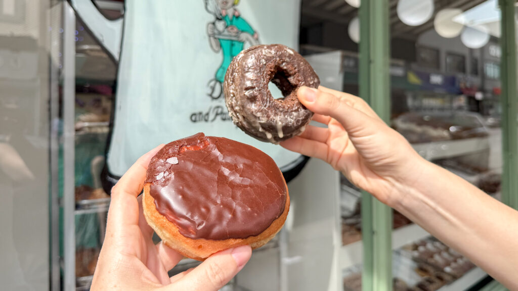 Peter Pan Donuts Brooklyn | Krista the Explorer Close-up of hands holding two chocolate-glazed donuts.