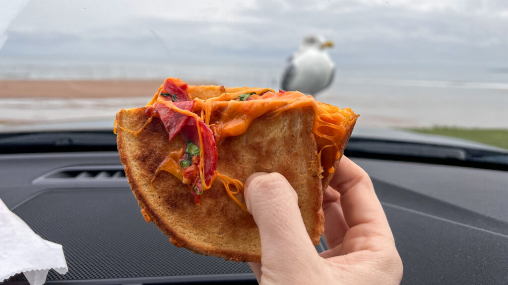Hand holding a toasted sandwich with melted orange cheese and pepperoni.