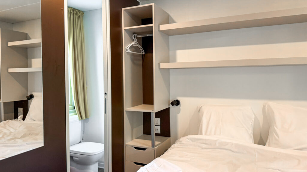 Compact hotel room with two single beds and an open wardrobe.