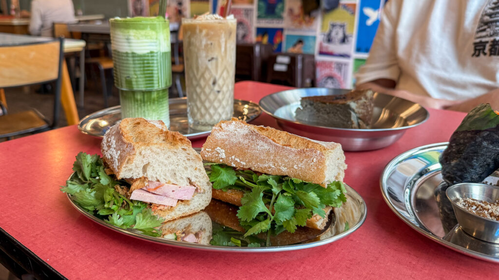 Nam Cà Phê Luxembourg | Krista the Explorer Sandwich on a baguette with ham and cilantro on a metal plate.
