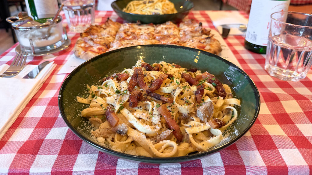 Cannoleria Luxembourg | Krista the Explorer Bowl of creamy pasta with bacon bits on a red-and-white checkered table.