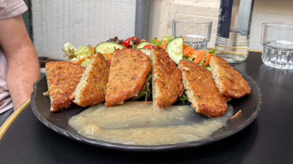 Golden brown breaded croquettes arranged on a black plate with a green salad.