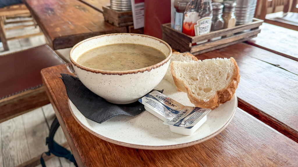Creamy soup in a speckled ceramic bowl with slices of white bread and butter packets.