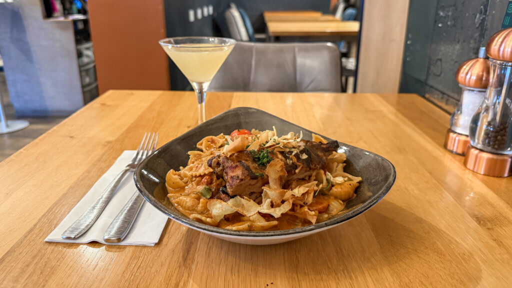 Pasta dish in a dark bowl topped with crispy onions and herbs on a wooden table.