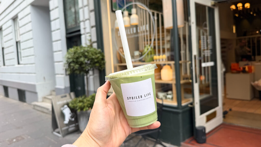 Person holding a green matcha latte in a clear cup outside cafe.