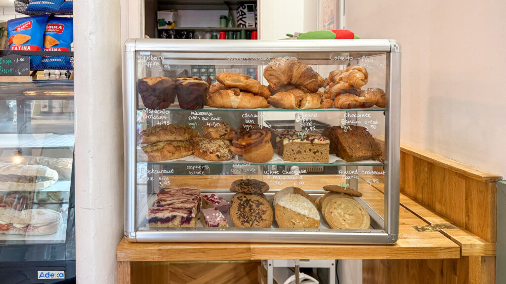 Display case filled with croissants, muffins, breads and cakes at a bakery shelf.