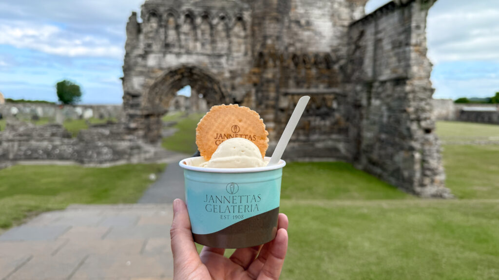Ice cream in a blue cup with a cookie and spoon held in front of medieval ruins
