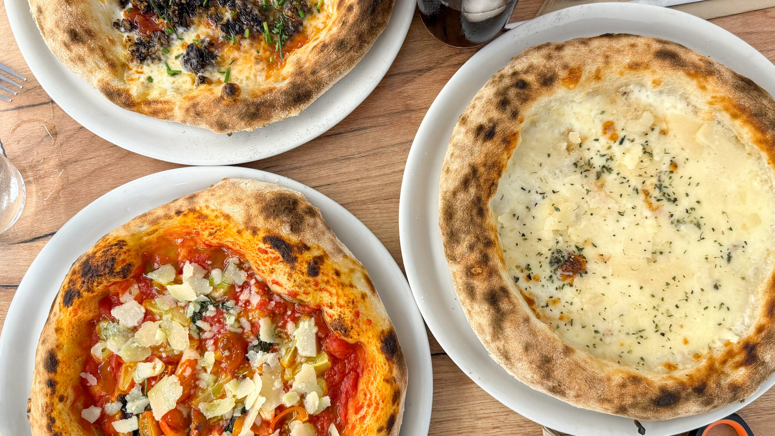Three freshly made pizzas on table in restaurant.