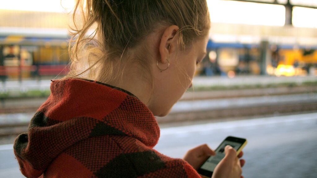 Woman looking at smartphone while walking on train platform.